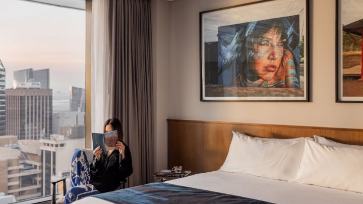 A guest reading a book in a hotel room with the curtains open showing a cityscape view